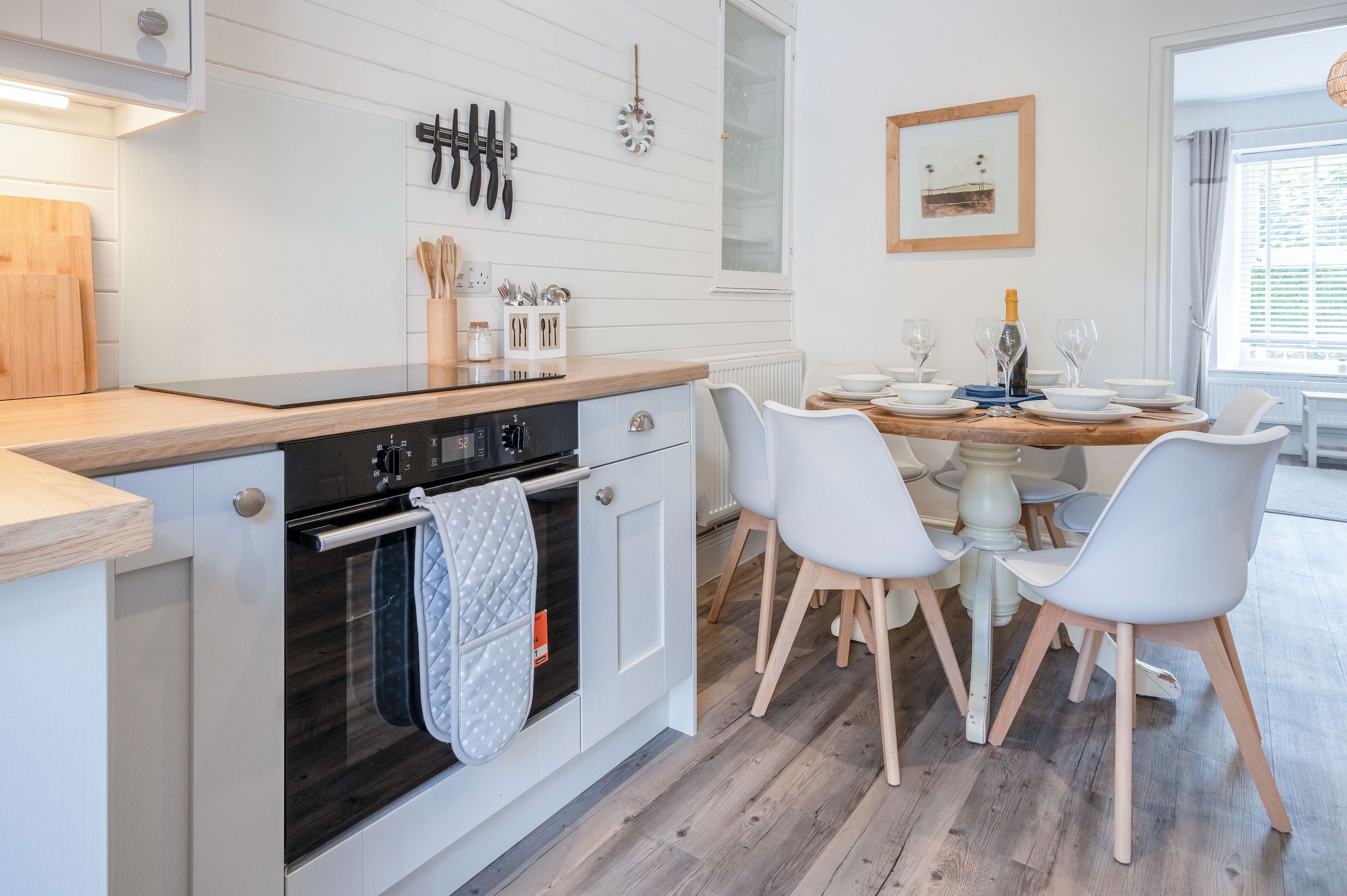 A modern kitchen with white cabinetry, a wooden countertop, and a dining area with white chairs and a wooden table.