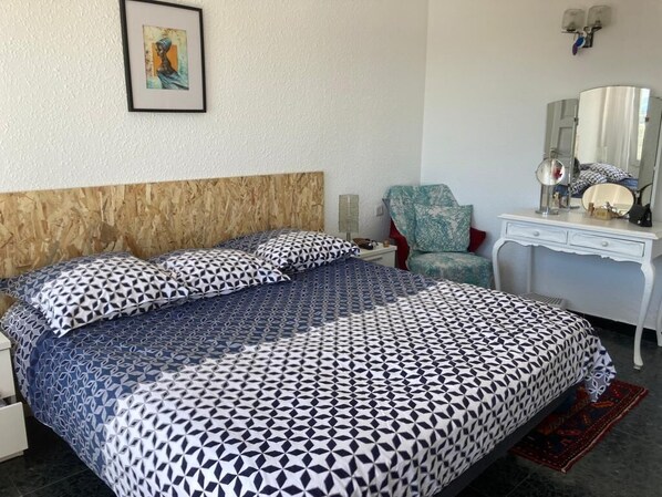 A bedroom with a patterned bedspread, a wooden headboard, a desk with a mirror, and a chair.