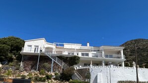 A multi-story white building with balconies, a staircase, and a view of a mountainous landscape.