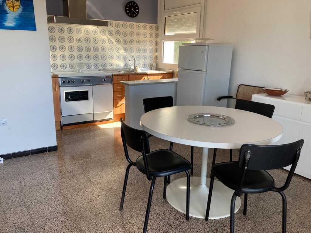 A compact kitchen with a round dining table, black chairs, a white refrigerator, and a stove.