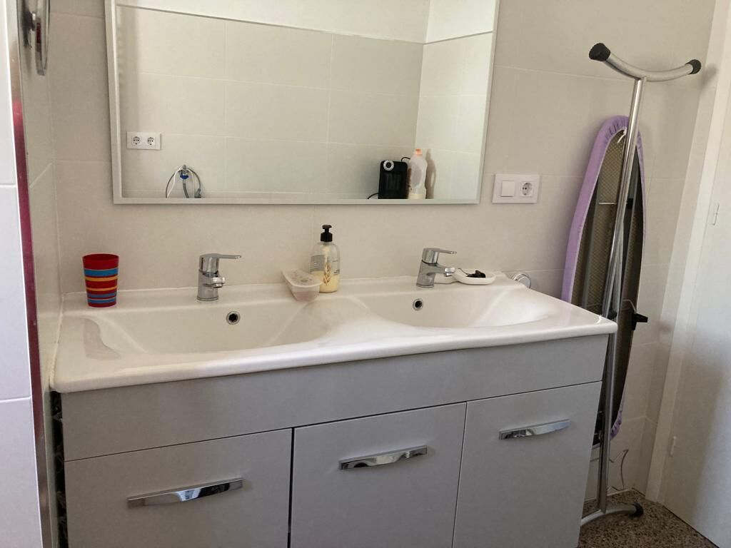 A bathroom with a white sink, two faucets, a mirror, and a towel rack.