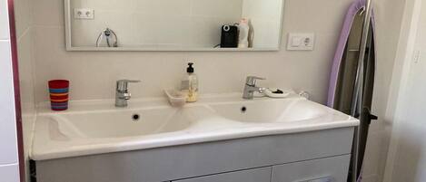 A bathroom with a white sink, two faucets, a mirror, and a towel rack.