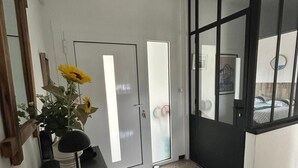 A hallway with a door, a mirror, a potted plant, and a black-framed window.