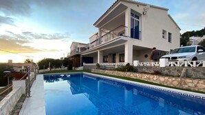 A two-story house with a swimming pool, a balcony, and a stone wall.