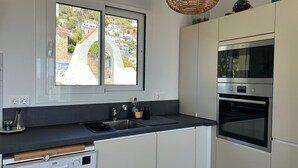 A modern kitchen with a built-in dishwasher, a double sink, and a large window offering a view of a bridge and buildings.