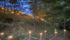 Un paseo marítimo de madera con barandas de cuerda, rodeado de árboles e iluminado con luces de adorno.