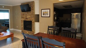 Een eetgedeelte met een houten tafel en stoelen, een stenen open haard, een flatscreen-televisie aan de muur en een keuken met moderne apparatuur.