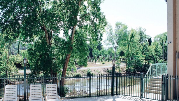 Een terras met twee witte loungestoelen, een metalen hek en uitzicht op een rivier en bomen.