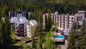 A resort with multiple buildings, a swimming pool, and a forested mountain backdrop. - Iron Horse C5013 Condo by RedAwning (Winter Park)