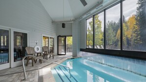 An indoor swimming pool with a view of trees through large windows, a poolside seating area, and a covered patio. - Iron Horse C5013 Condo by RedAwning (Winter Park)