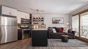 A modern kitchen with stainless steel appliances, a central island, and a dining area with a dark-colored sofa and a small round table. - Iron Horse C3013 Condo by RedAwning (Winter Park)