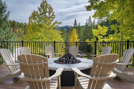 A deck with Adirondack chairs and a stone fire pit surrounded by a black metal railing.
