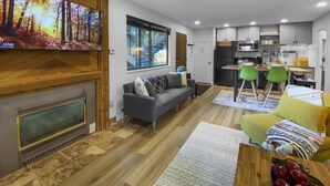 Uma sala de estar moderna com lareira, um sofá e um espaço de jantar com cadeiras verdes.