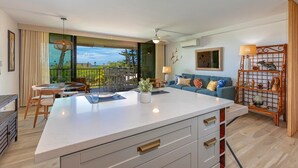 Una cocina moderna con una isla grande, comedor con mesa y sillas, un sofá y una estantería decorativa.