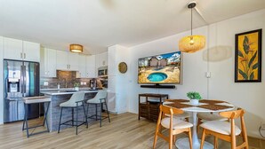 Una cocina moderna con armarios blancos, una isla integrada y una zona de comedor con mesa redonda y sillas de madera.