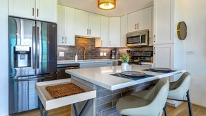 Una cocina moderna con gabinetes blancos, electrodomésticos de acero inoxidable y una isla central con taburetes de bar.