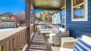 A covered outdoor patio with wicker furniture, a wooden deck, and a view of neighboring houses and trees.