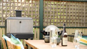 Ein Grill mit digitalem Thermometer, ein Tisch mit Flasche und Gläsern sowie ein Holzstuhl.