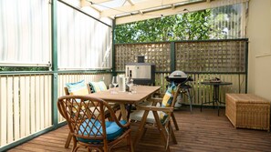 En udendørs terrasse med et træbord, fletstole, en grill og et lille rundt bord.