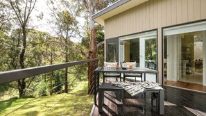 A modern outdoor deck with a table and chairs, overlooking a forested area. - Wyuna (Hepburn Springs)