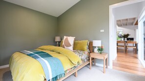 A bedroom with a bed, bedside lamps, a nightstand, and a view into the kitchen. - Wyuna (Hepburn Springs)
