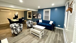 Ein Wohnzimmer mit blauer Wand, ein Essbereich mit Tisch und Stühlen sowie eine Decke mit Einbuchtungslampen.