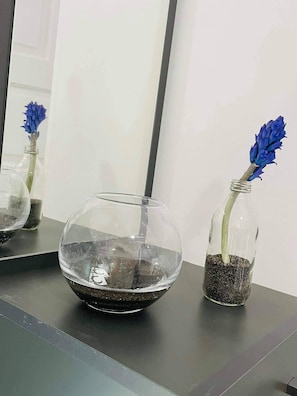 Two glass vases with blue flowers and soil on a reflective surface.