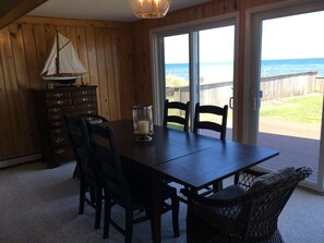 Ein Esszimmer mit Holzboden, einem Tisch und Stühlen, einer Kommode und Meerblick durch große Schiebeglastüren.