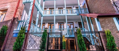 A two-story building with a balcony, potted plants, and a gated entrance.