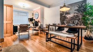 Una sala moderna con piso de madera, una mesa de comedor con cuatro sillas, un banco y un cuadro grande con una escena tropical.
