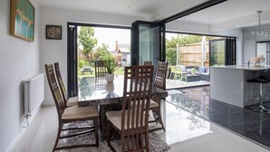 A dining area with a glass table and chairs, a view of the backyard, and a kitchen area with a modern design.