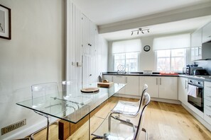 A modern kitchen with white cabinets, a glass dining table, and a wooden floor.