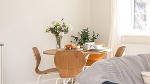 Un comedor con una mesa redonda, sillas, un florero con flores y una ventana con vistas.