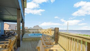 A wooden deck with a hot tub, wooden chairs, and a view of the beach.