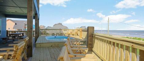 A wooden deck with a hot tub, wooden chairs, and a view of the beach.