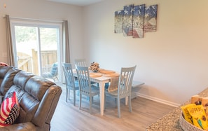 A dining area with a white table and chairs, a leather couch with an American flag pillow, and a wooden fence visible through the glass door.