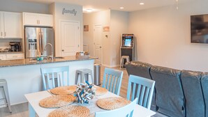A modern kitchen with white cabinets, a stainless steel refrigerator, and a dining area with blue chairs and woven placemats. - Clean New Townhome: Comfort and Convenience Await! (Hampstead)