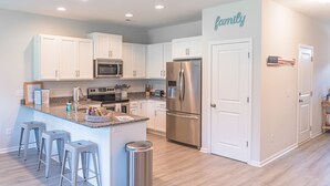 A modern kitchen with white cabinets, stainless steel appliances, and a central island with stools. - Clean New Townhome: Comfort and Convenience Await! (Hampstead)