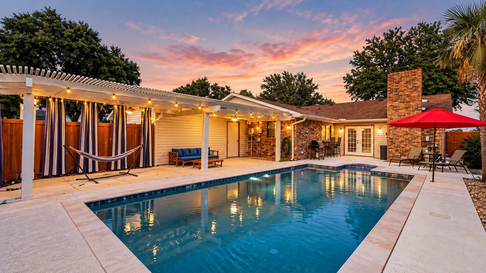 A swimming pool with a covered patio area, outdoor furniture, and a brick wall.