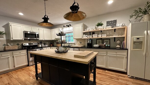A modern kitchen with white cabinets, a central island, stainless steel appliances, and pendant lighting.