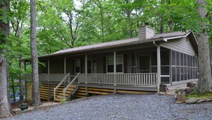 A cabin with a porch, wooden steps, and a gravel driveway.