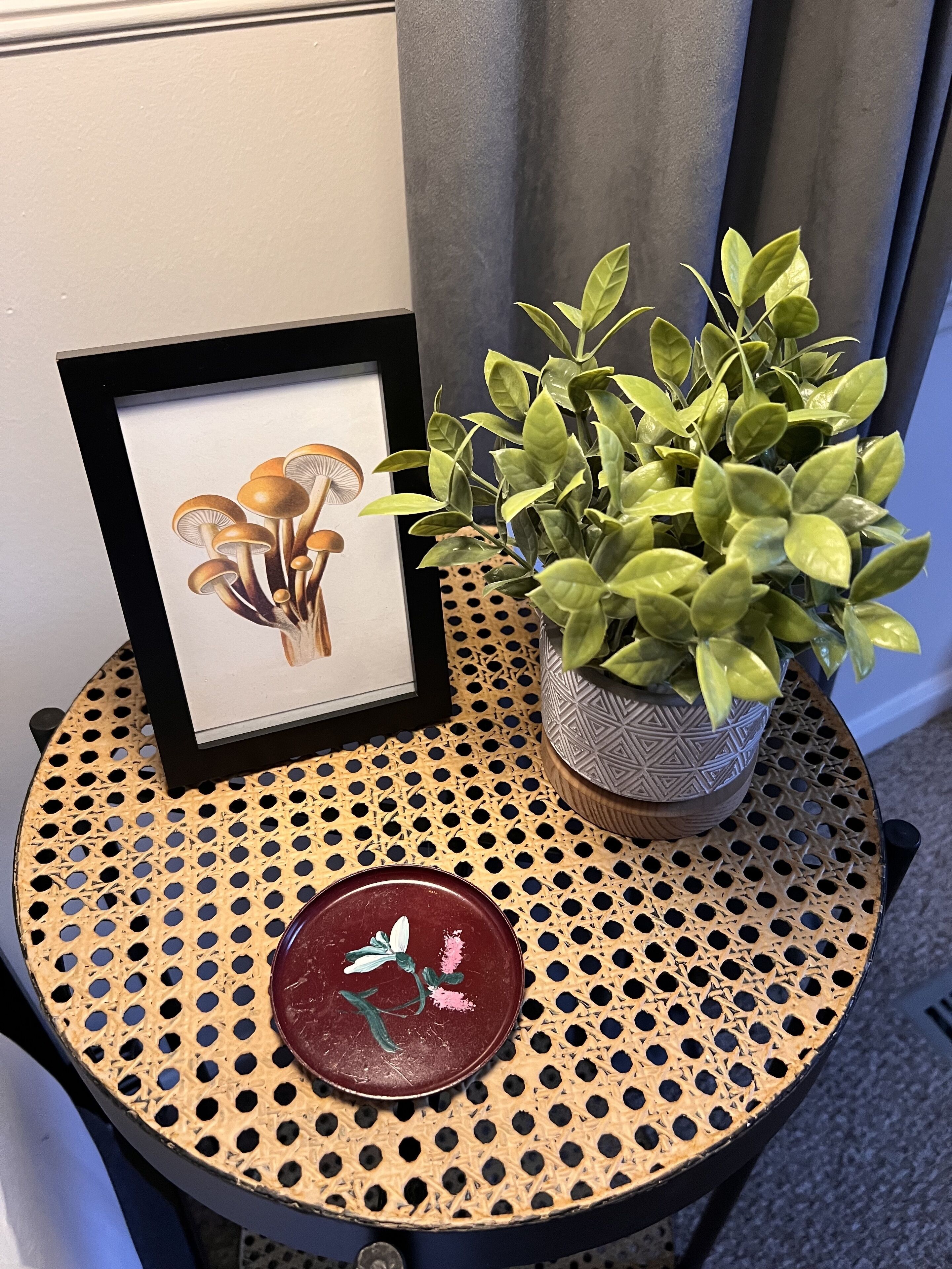 A framed artwork of mushrooms, a potted plant, and a decorative plate on a round table.