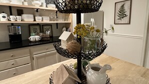 A three-tiered black metal stand with a white pitcher and a small birdhouse on the bottom tier.