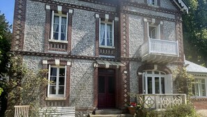 A two-story stone building with a red door, multiple windows, and a small balcony.
