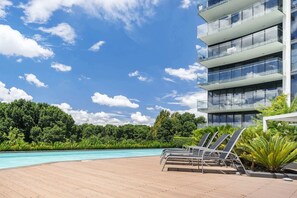 A modern hotel with a pool area, including lounge chairs and a clear view of the surrounding greenery.