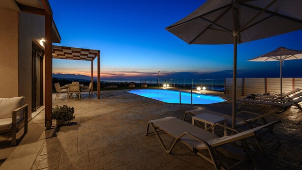 A rooftop pool area with lounge chairs, umbrellas, and a view of the ocean at dusk. - Jason Panorama 1 Villa (Rethymno)