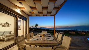 A dining area with a table set for four, overlooking a scenic view of the ocean at dusk. - Jason Panorama 1 Villa (Rethymno)