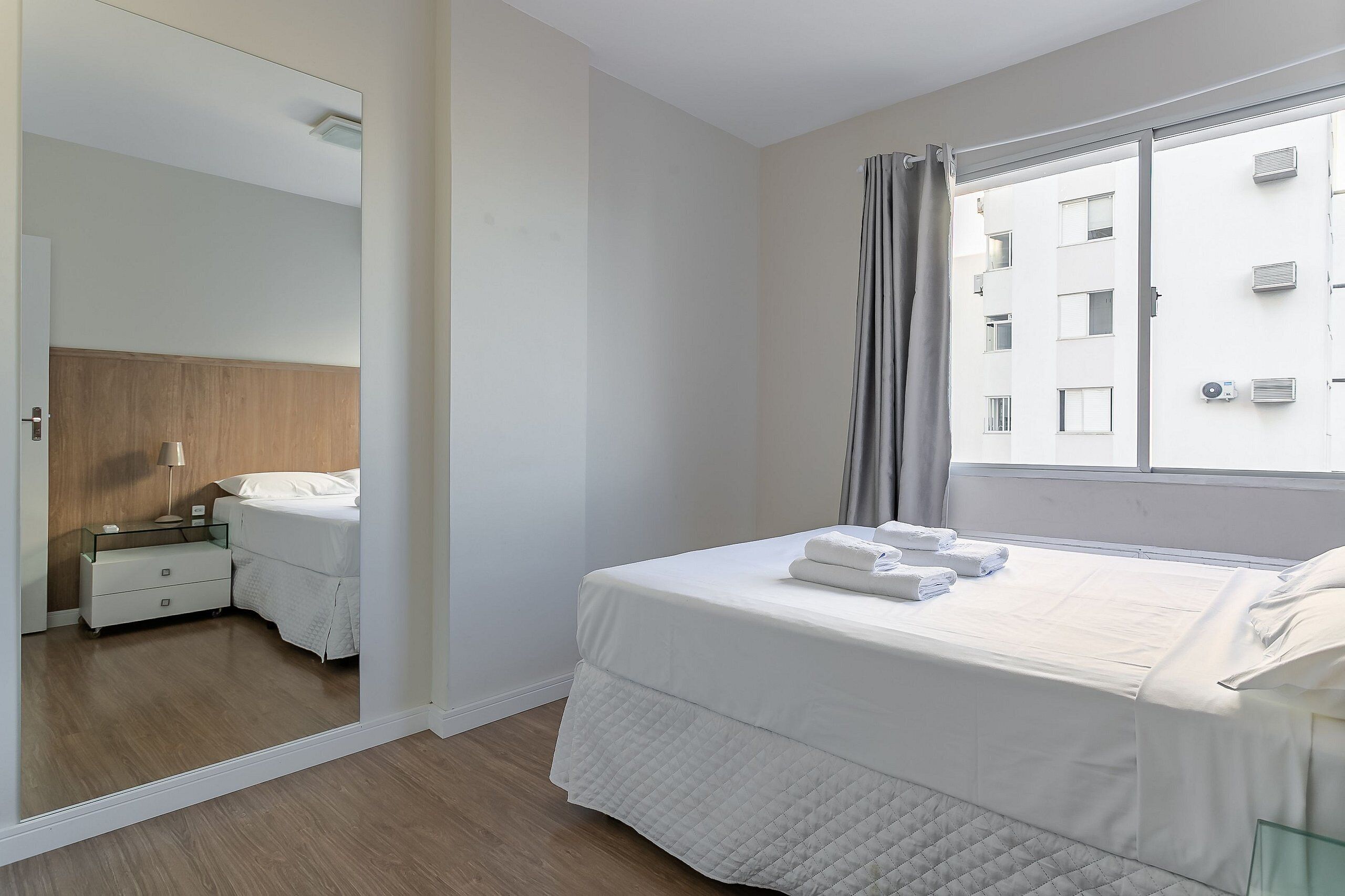 A hotel room with a bed, a nightstand, a mirror, and a window with curtains.
