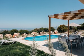 Un área junto a la piscina con pérgola, sillas de descanso y una mesa con sillas.