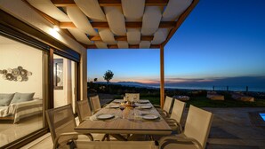A dining area with a table set for four, overlooking a scenic view of the ocean at dusk.